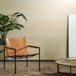 Moderne interieurhoek met een leren stoel, kamerplant, ronde tafel en Arte-behang uit de Expedition Tasar-collectie op de achtergrond.