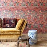 Kleurrijk interieur met Arte Gitane Emperador behang, een fluwelen gele bank en etnische decoratieve accenten.