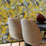 Twee beige stoelen aan een zwarte tafel met op de achtergrond geel Arte-behang Insolence Grow met een weelderig bloemenpatroon.