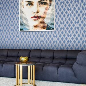 Blauw Arte-behang uit de Insolence Moxie collectie met een geometrisch patroon, achter een donkerblauwe bank en een moderne kunstfoto aan de muur.