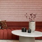 Moderne zithoek met rood Arte-behang Insolence Shiver, een ronde marmeren tafel en decoratieve vaas.
