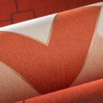 Close-up van het Arte-behang Insolence Vanity met een grafisch patroon in oranje, goud en beige tinten.
