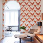 Moderne woonkamer met Arte-behang Insolence Vanity2 in oranje visgraatpatroon en een comfortabele loungestoel met poef.