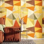 Kleurrijk Arte-behang JV800 Tierra Savana 6633 met geometrisch patroon in warme aardetinten achter een roestbruine stoel en bijzettafel met decoratieve vaas.