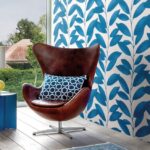Bruine designstoel met blauw sierkussen voor een muur met blauw-wit Arte-behang uit de Joy Blooming Marvellous-collectie.