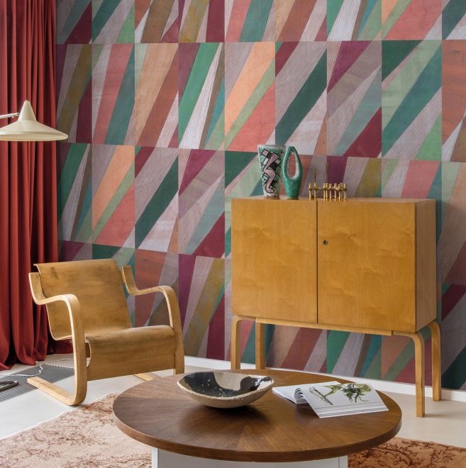 Interieur met Arte-behang Joy Print in kleurig geometrisch patroon, houten meubels en rode gordijnen.