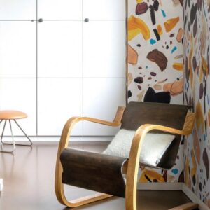 Houten schommelstoel in een moderne kamer met kleurrijk Arte Joy Terrific Terrazzo-behang op de muur.