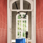 Stijlvolle gang met Arte behang uit de Kanso Iki 72510 collectie in rood en grijs, moderne verlichting en blauwe zitpoefs.