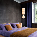 Sfeervolle slaapkamer met Arte-behang Kanso Shibumi 72532, een paarse sprei, okergele accenten en moderne hanglamp.