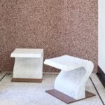 Twee marmeren bijzettafels staan op een mozaïekvloer voor een wand met rood gespikkeld Arte Kharga behang in de kleur Flaming Red.