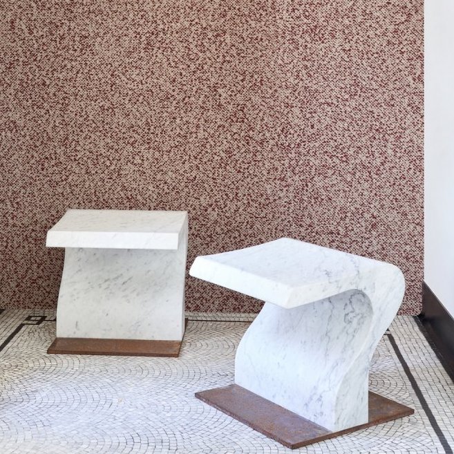 Twee marmeren bijzettafels staan op een mozaïekvloer voor een wand met rood gespikkeld Arte Kharga behang in de kleur Flaming Red.