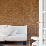 Woonkamer met Arte Kharga Barkhan 74001 ochre behang en een witte bank met kussens.