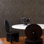 Moderne interieursetting met Arte-behang Kharga Gobi, een ronde witte tafel, sculpturale zwarte stoelen en een decoratieve vaas.