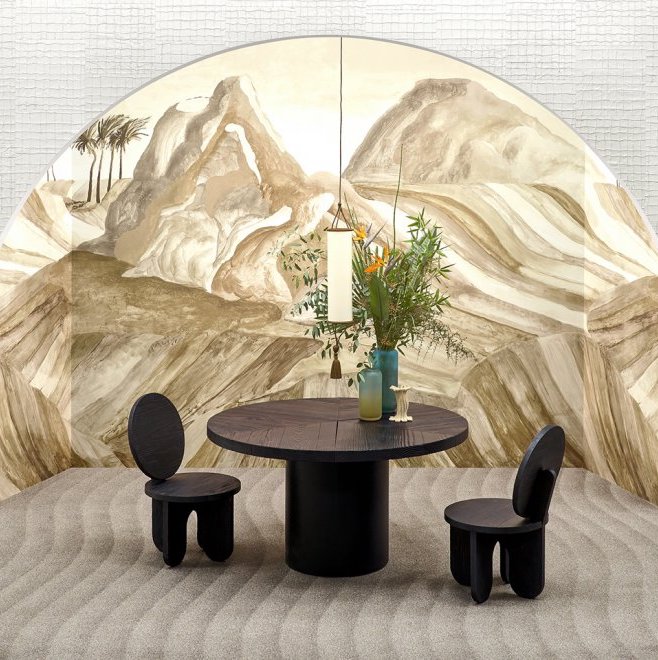 Ronde zwarte eettafel met twee stoelen voor een muur met het panoramische Arte-behang Kharga Zerzura in aardetinten met duinlandschap.