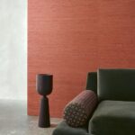 Groene fluwelen bank met sierkussen voor een muur bekleed met rood Arte-behang Kudzu 54536.