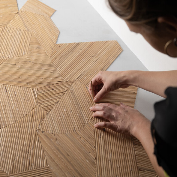 Persoon plaatst met de hand een stuk Arte-behang in Lanai-techniek met een geometrisch patroon van fijne bamboestructuren.