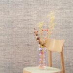 Vaas met gedroogde bloemen op een houten stoel tegen Arte-behang Le Papier Tissé Buningh.