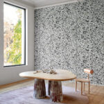 Moderne interieursetting met Arte-behang La Perle 58530 met zwart-wit botanisch motief, houten tafel en designstoel.