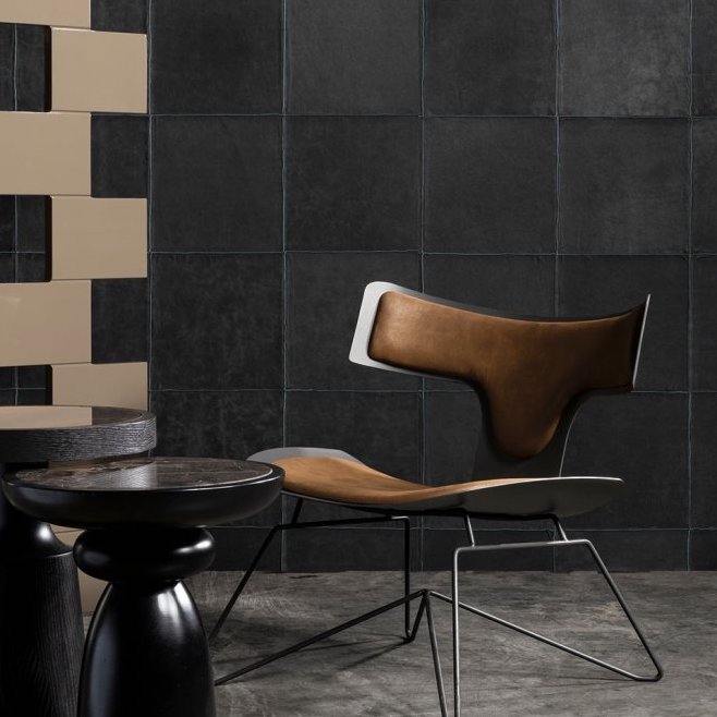 Designstoel met leren bekleding voor een muur met donker Arte-behang uit de Les Cuirs Aspect4-collectie.