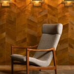 Grijze designfauteuil voor een wand met Arte-behang uit de Les Cuirs-collectie in warme bruintinten.