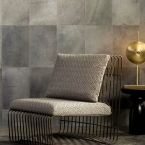 Designstoel met metalen frame en zacht kussen staat voor een muur bekleed met Arte-behang Les Cuirs Rectangle.