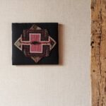 Textielkunst met etnisch patroon aan de muur met licht structuurbehang uit de Arte Nongo behangcollectie.