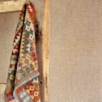 Kleurrijk, etnisch geïnspireerd kleedje hangt over een houten ladder tegen het Nongo-behang uit de Gitane-collectie van Arte.