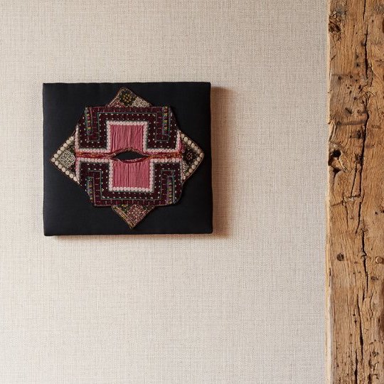 Textielkunst met etnisch patroon aan de muur met licht structuurbehang uit de Arte Nongo behangcollectie.