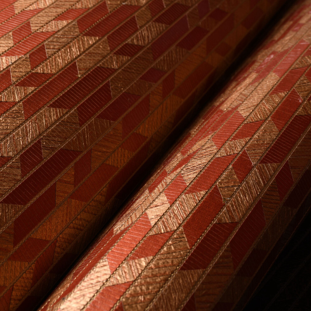 Detailopname van Arte behang Papyrus 48552 met een geometrisch patroon in rood- en koperkleurige tinten.