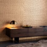 Moderne woonkamer met Arte Papyrus-behang in goudtinten, een donkere houten kast en een stijlvolle messing tafellamp.