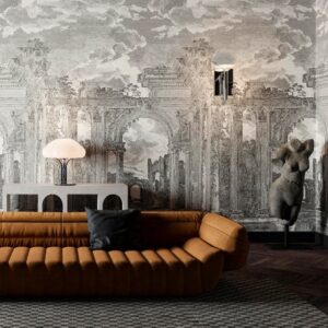 Moderne woonkamer met okerkleurige bank en Arte-behang 'Rovine Buningh' met een klassieke ruïneprint op de achtergrond.
