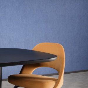 Moderne interieurhoek met blauw Arte Temper behang, een oranje designstoel en een zwarte ovale tafel.