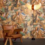 Bruin Arte Terra Tropicana behang met tropisch patroon, gecombineerd met een leren stoel en een decoratieve staande lamp.