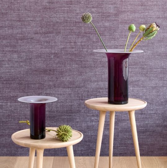 Twee paarse vazen met bloemen staan op houten bijzettafels voor een paars Arte Textura Canvas behang.