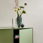 Groene kast met een vaas met bloemen, kandelaars en een potje tegen een Arte Textura Marsh 31501A behang.