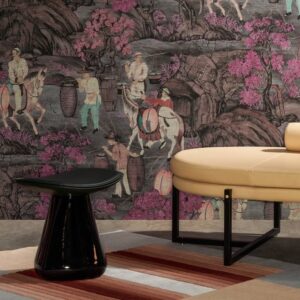 Beeld van een interieur met een panoramisch roze Arte-behang uit de Toile de Tibet collectie, met Aziatische taferelen, een ronde beige bank en een zwarte bijzettafel op een gestreept vloerkleed.