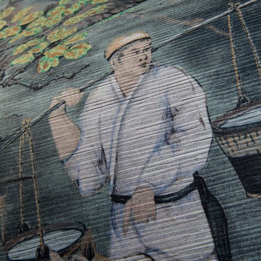 Detail van groen Arte-behang uit de Toile de Tibet collectie met een geschilderde figuur die manden draagt.