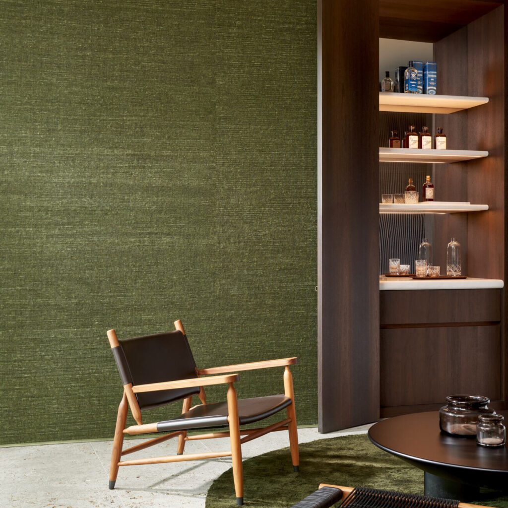 Moderne zithoek met een groene Arte WildSilk KatiaSilk 86503 behangwand, houten loungefauteuil en stijlvolle open drankkast.