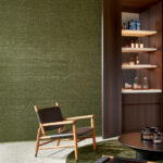 Moderne zithoek met een groene Arte WildSilk KatiaSilk 86503 behangwand, houten loungefauteuil en stijlvolle open drankkast.