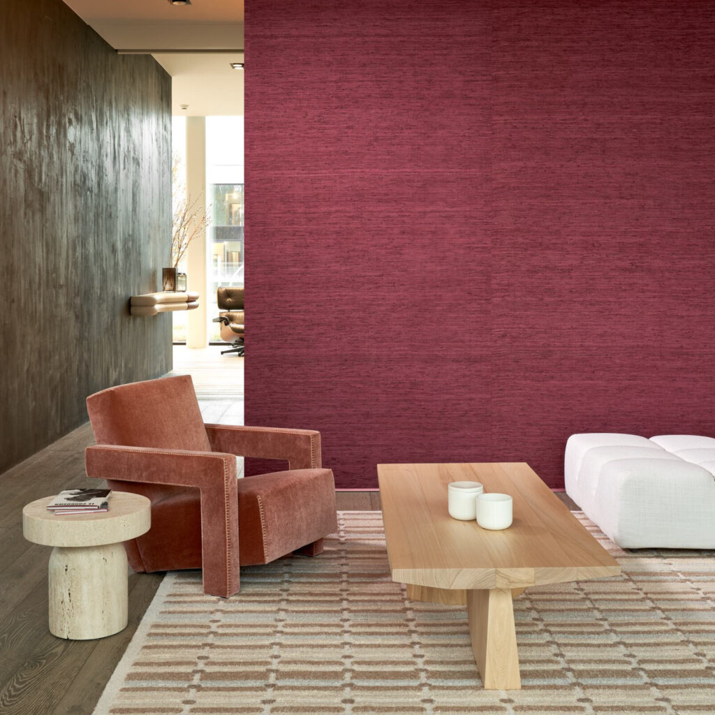 Moderne zithoek met Arte Wild Silk behang in diepe bordeauxkleur, een velvet fauteuil, houten salontafel en geometrisch vloerkleed.