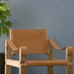 Lederen designstoel met houten frame voor een Arte Wildwalk Ferox1-behang met subtiel patroon.