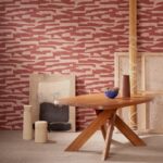 Hedendaags interieur met Arte-behang Essentials Costura Gabarit 57563 in rood en beige patroon, houten tafel en decoratieve objecten.