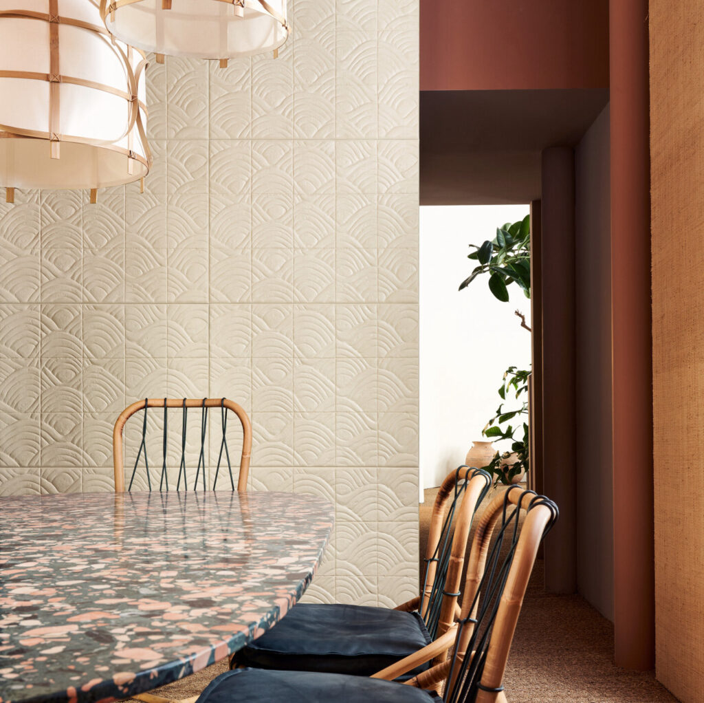 Eetkamer met Babylon Terracotta wandtegels, een ovale terrazzo eettafel en rotanstoelen met donkerblauwe kussens.