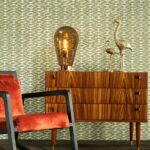 Retro interieuropstelling met Behang Essentials Travellers Calanco, houten dressoir, fluwelen stoel en decoratieve accessoires.