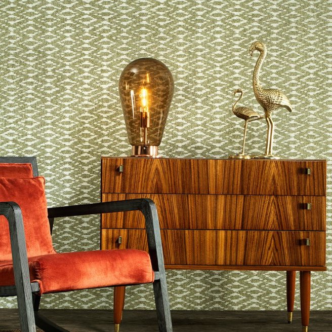Retro interieuropstelling met Behang Essentials Travellers Calanco, houten dressoir, fluwelen stoel en decoratieve accessoires.