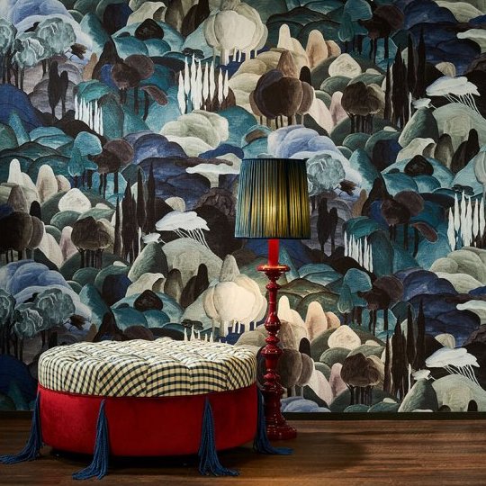 Rijke interieursetting met Arte-behang 'Allombra dei cipressi', een rode ottoman en een klassieke rode lamp met blauwgroene kap.