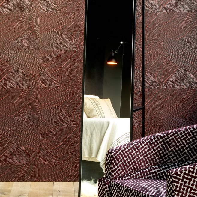 Kamer met Arte behang Arado Rose Brown, een spiegel die een bed reflecteert, en een stoel met grafisch patroon op de voorgrond.