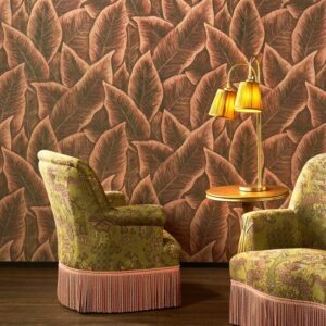 Twee klassieke fauteuils en een bijzettafel met lamp staan voor behang met tropisch bladerpatroon uit de Arte Bird of Paradise-collectie.