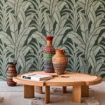 Ronde houten tafel met drie kleurrijke rieten vazen en een boek, voor een groene botanische Arte-behangwand.