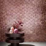 Ronde houten tafel met vaasjes staat voor een glanzende roze muur met Arte Camber behang in waaiervormig patroon.